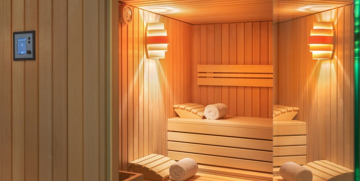 A modern sauna with wooden benches, towels, and soft lighting. A thermometer is mounted on the wall., &copy; Novum Hospitality