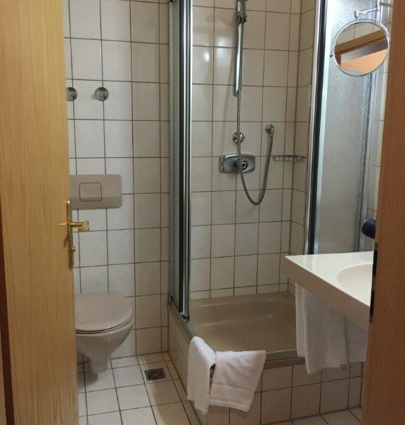 Small bathroom with shower, toilet and washbasin. White tiles, towel on the shower cubicle, round mirror on the wall., © TOMAS