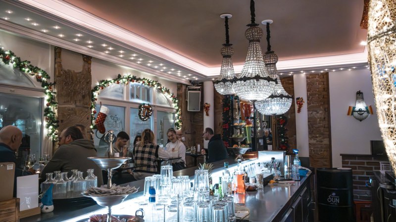 Festively decorated bar with chandeliers, guests at the bar and Christmas decorations. Glasses and bottles on the bar., © SMG Stuttgart Marketing GmbH - Sarah Schmid Festively decorated bar with chandeliers, guests at the bar and Christmas decorations. Glasses and bottles on the bar., © SMG Stuttgart Marketing GmbH - Sarah Schmid