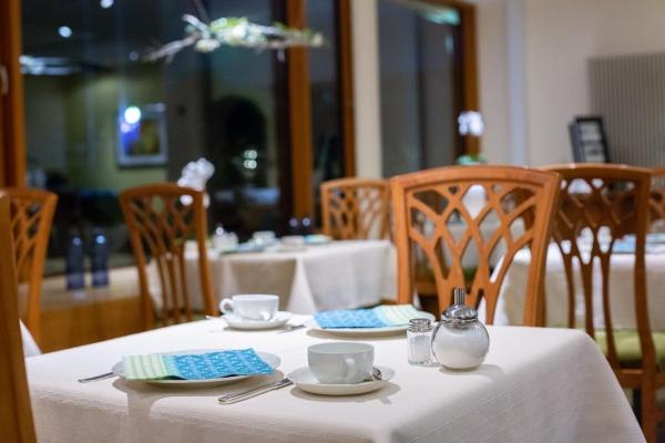 Ein eleganter Frühstücksraum mit gedeckten Tischen, Tassen, Besteck und Servietten. Holzmöbel und große Fenster sorgen für eine einladende Atmosphäre., © Kronen Hotel GmbH Ein eleganter Frühstücksraum mit gedeckten Tischen, Tassen, Besteck und Servietten. Holzmöbel und große Fenster sorgen für eine einladende Atmosphäre., © Kronen Hotel GmbH