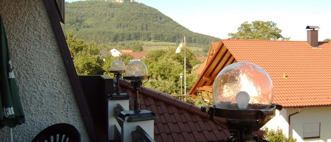 Blick von einem Balkon mit Lampen auf eine Burg auf einem bewaldeten Hügel. Im Vordergrund sind Dächer und ein Garten zu sehen., © Hotel & Restaurant Beurener Hof Blick von einem Balkon mit Lampen auf eine Burg auf einem bewaldeten Hügel. Im Vordergrund sind Dächer und ein Garten zu sehen., © Hotel & Restaurant Beurener Hof