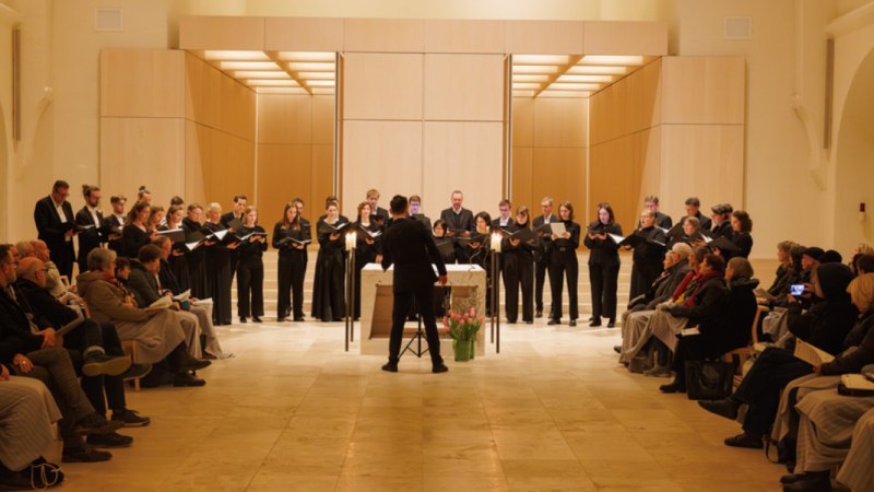 Ein Chor singt in einer Kirche, dirigiert von einer Person. Das Publikum sitzt auf beiden Seiten und hört zu. Die Atmosphäre ist feierlich., © Heiko Tiedmann