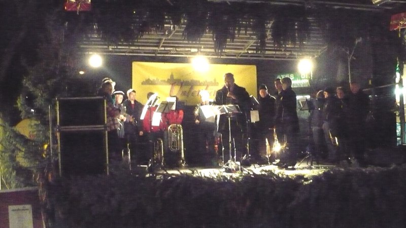 Eine Musikgruppe spielt auf einer festlich dekorierten Bühne in Untertürkheim. Die Bühne ist mit Lichtern und Tannenzweigen geschmückt., © Foto: Enslin Eine Musikgruppe spielt auf einer festlich dekorierten Bühne in Untertürkheim. Die Bühne ist mit Lichtern und Tannenzweigen geschmückt., © Foto: Enslin