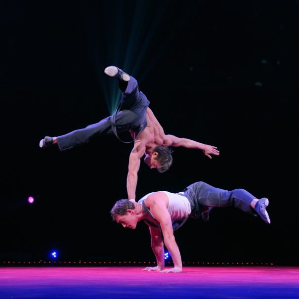 Zwei Artisten zeigen eine beeindruckende akrobatische Performance auf einer Zirkusb&uuml;hne. Einer balanciert auf den H&auml;nden, w&auml;hrend der andere auf dessen Hals balanciert., &copy; Foto Thierry Bissat