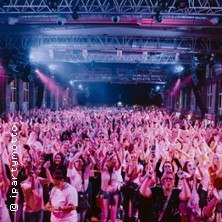 Konzertbesucher in einer großen Halle feiern mit erhobenen Händen. Die Bühne ist im Hintergrund, bunte Lichter erhellen die Szene., © links im Bild Konzertbesucher in einer großen Halle feiern mit erhobenen Händen. Die Bühne ist im Hintergrund, bunte Lichter erhellen die Szene., © links im Bild