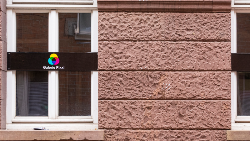 Zwei Fenster mit Schildern der Galerie Pixxl an einer roten Backsteinwand. Die Schilder zeigen ein buntes Logo und den Namen der Galerie., &copy; Stuttgart-Marketing GmbH, Sarah Schmid