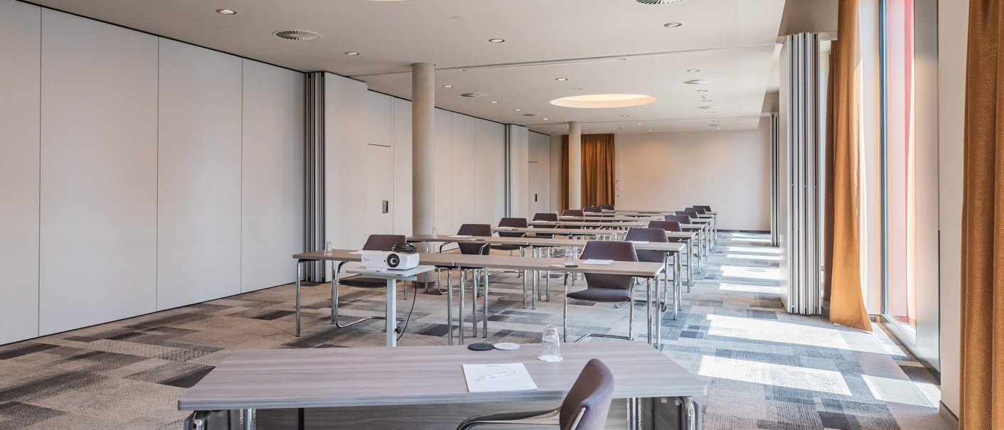 Moderner Konferenzraum mit Tischen, Stühlen, Deckenbeleuchtung und großen Fenstern im Hilton Garden Inn., © Hilton Garden Inn Stuttgart Neckarpark