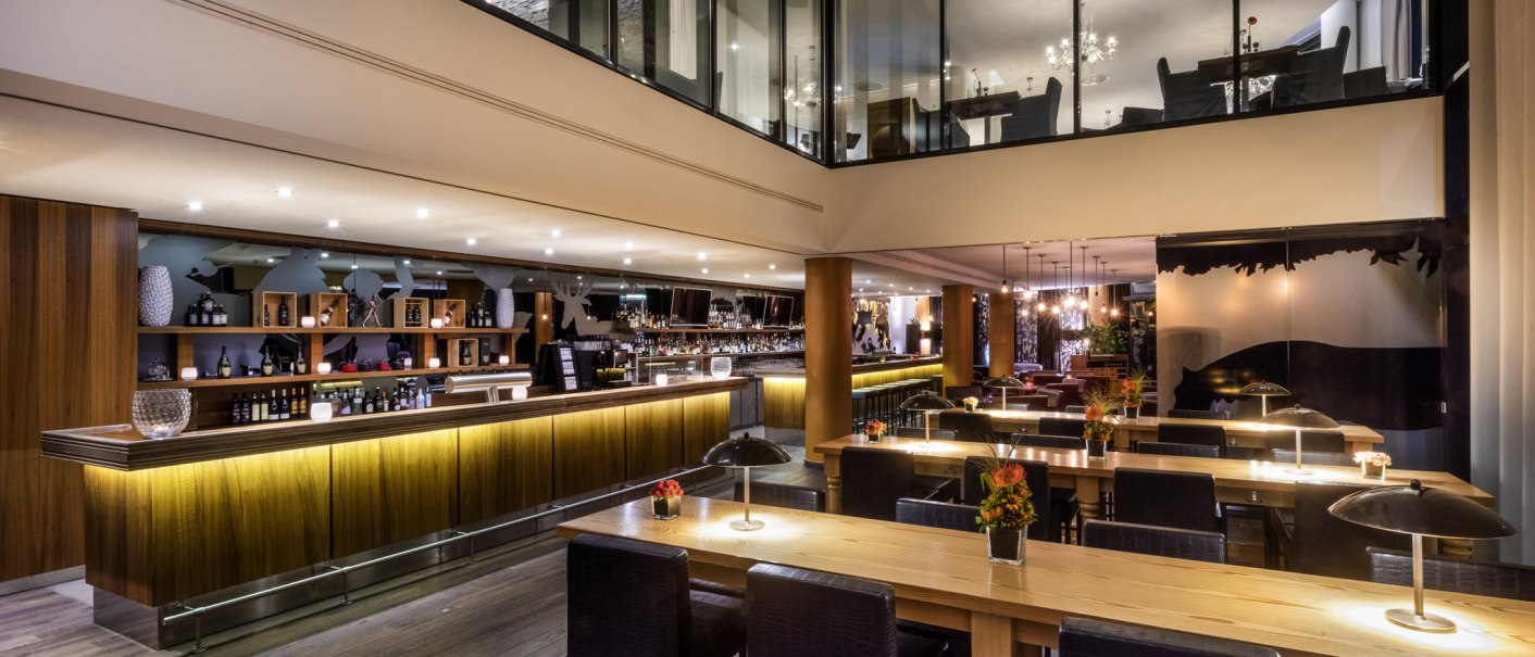 Moderne Bar mit eleganter Holztheke, stilvoller Beleuchtung und gemütlichen Sitzbereichen. Obergeschoss mit Glaswänden und Kronleuchtern., © Mövenpick Hotel Stuttgart Airport Moderne Bar mit eleganter Holztheke, stilvoller Beleuchtung und gemütlichen Sitzbereichen. Obergeschoss mit Glaswänden und Kronleuchtern., © Mövenpick Hotel Stuttgart Airport