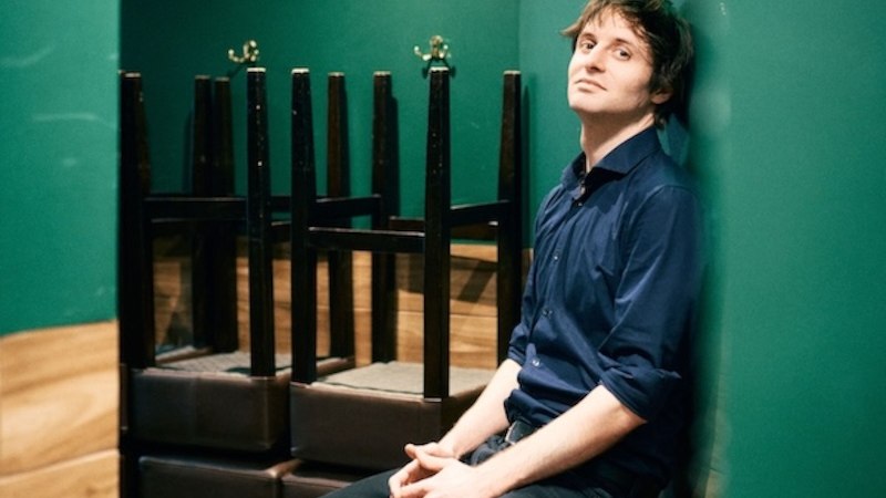 A man with brown hair and a blue shirt smiles at the camera in front of a neutral background., &copy; Renitenztheater Stuttgart e.V.