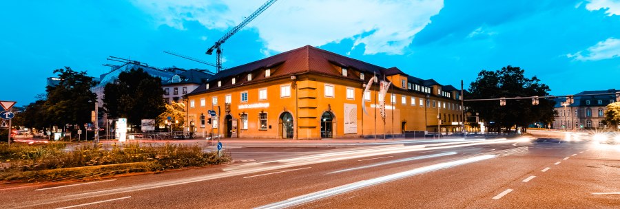 Yellow building at dusk, illuminated by streetlights. Cars leave light trails on the road, construction cranes in the background., &copy; &copy;Luca Siermann