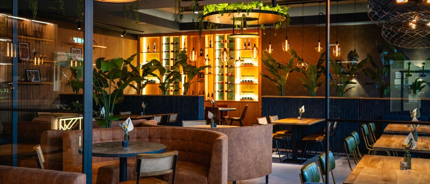 A stylish dining room with modern furniture, plants and warm lighting. Wooden tables and leather seats create an inviting atmosphere., © SatzDrei