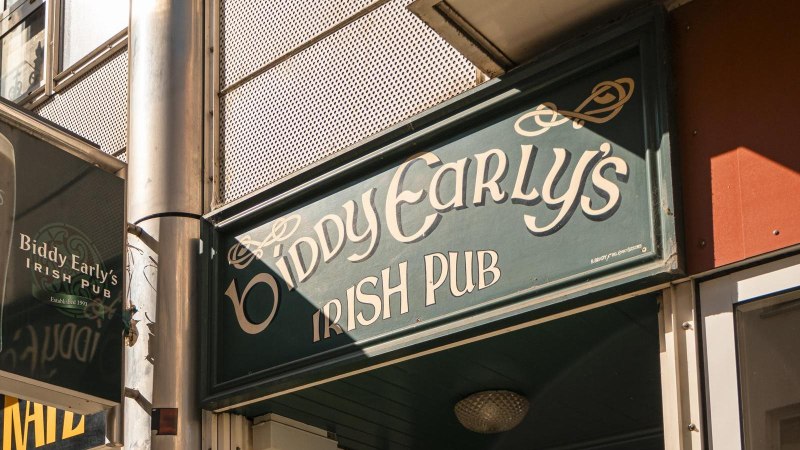 Eingang von Biddy Early's Irish Pub mit grünem Schild und Guinness-Werbung. Sonneneinstrahlung auf der Fassade., © SMG, Sarah Schmid