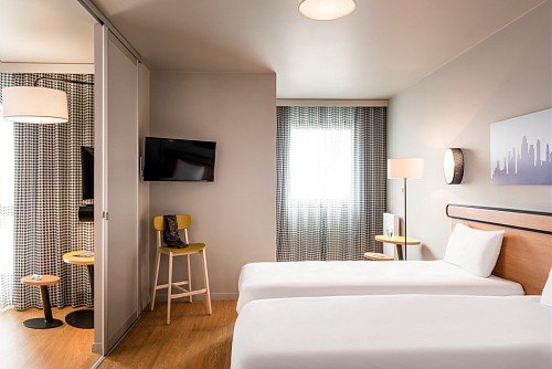 Modern hotel room with two single beds, TV, table and chair. A curtain separates the sleeping area from the seating area., &copy; adagio access Stuttgart Airport Messe