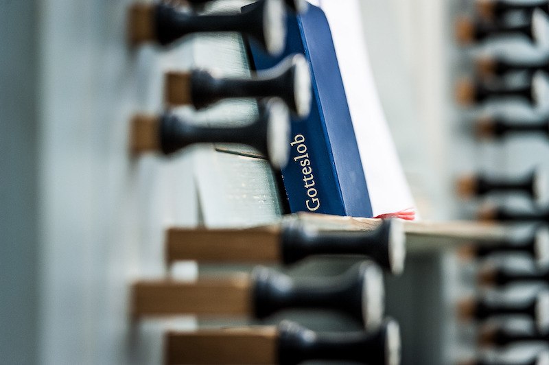 Ein Gotteslob-Buch steckt zwischen den Registern einer Orgel. Die Aufnahme fokussiert auf die Registerz&uuml;ge und das Buch., &copy; Staatliche Hochschule f&uuml;r Musik und Darstellende Kunst