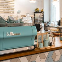 Modernes Café mit blauer Kaffeemaschine, dekorativen Fliesen und Backwaren. Helle, einladende Atmosphäre mit Pflanzen und Zeitschriften., © Stuttgart-Marketing GmbH, Sarah Schmid
