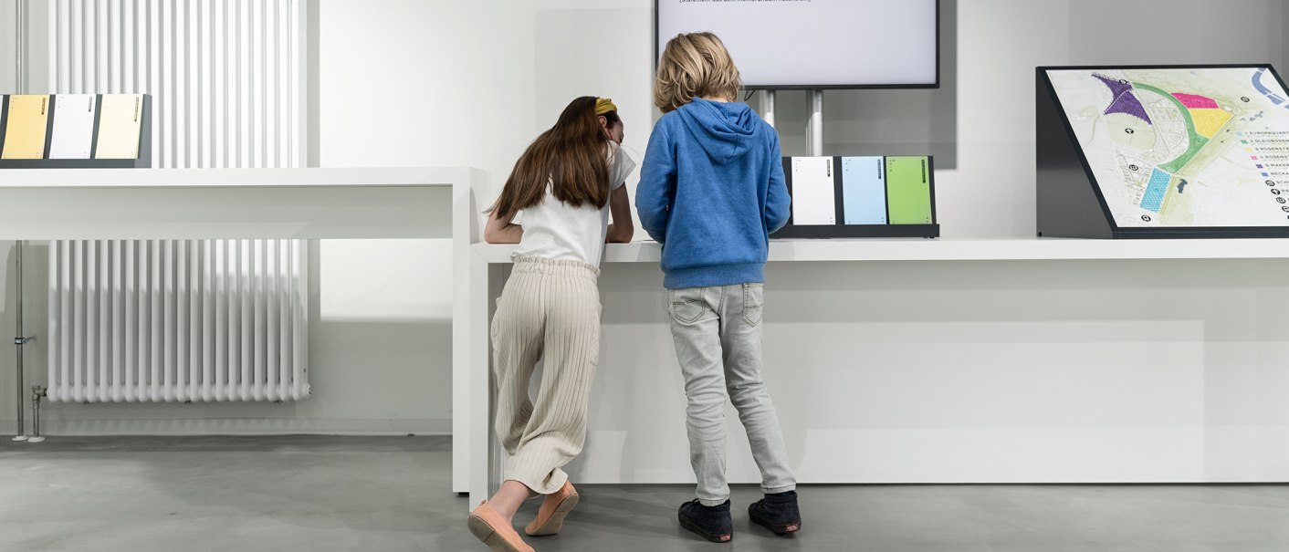 Two children look at an exhibition board in a modern room with white walls and a radiator., © Dominique Brewing Two children look at an exhibition board in a modern room with white walls and a radiator., © Dominique Brewing