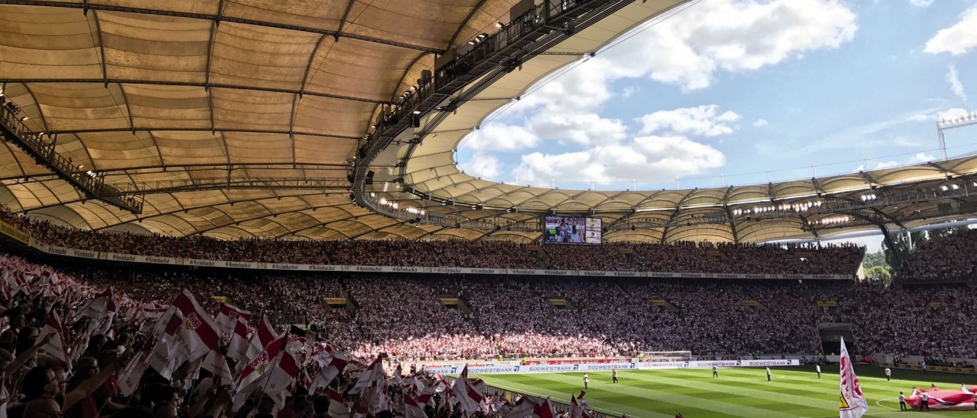 Die Mercedes-Benz Arena in Stuttgart, voll besetzt mit Fans, die Fahnen schwenken. Das Stadiondach ist gut sichtbar, der Himmel ist blau mit Wolken., &copy; Stuttgart-Marketing GmbH