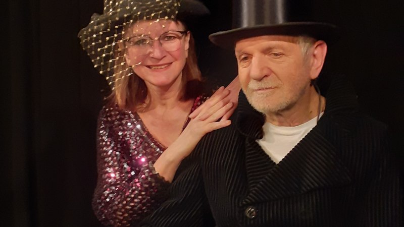 Ein Mann mit Zylinder und eine Frau mit Hut und Brille l&auml;cheln in die Kamera. Sie tr&auml;gt ein glitzerndes Oberteil, er einen dunklen Mantel., &copy; Helen Pavel