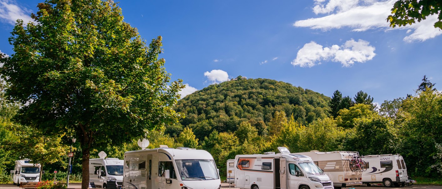 Wohnmobilstellplatz mit mehreren Wohnmobilen, umgeben von Bäumen und einem bewaldeten Hügel im Hintergrund unter blauem Himmel., © Stuttgart-Marketing GmbH, Thomas Niedermüller Wohnmobilstellplatz mit mehreren Wohnmobilen, umgeben von Bäumen und einem bewaldeten Hügel im Hintergrund unter blauem Himmel., © Stuttgart-Marketing GmbH, Thomas Niedermüller