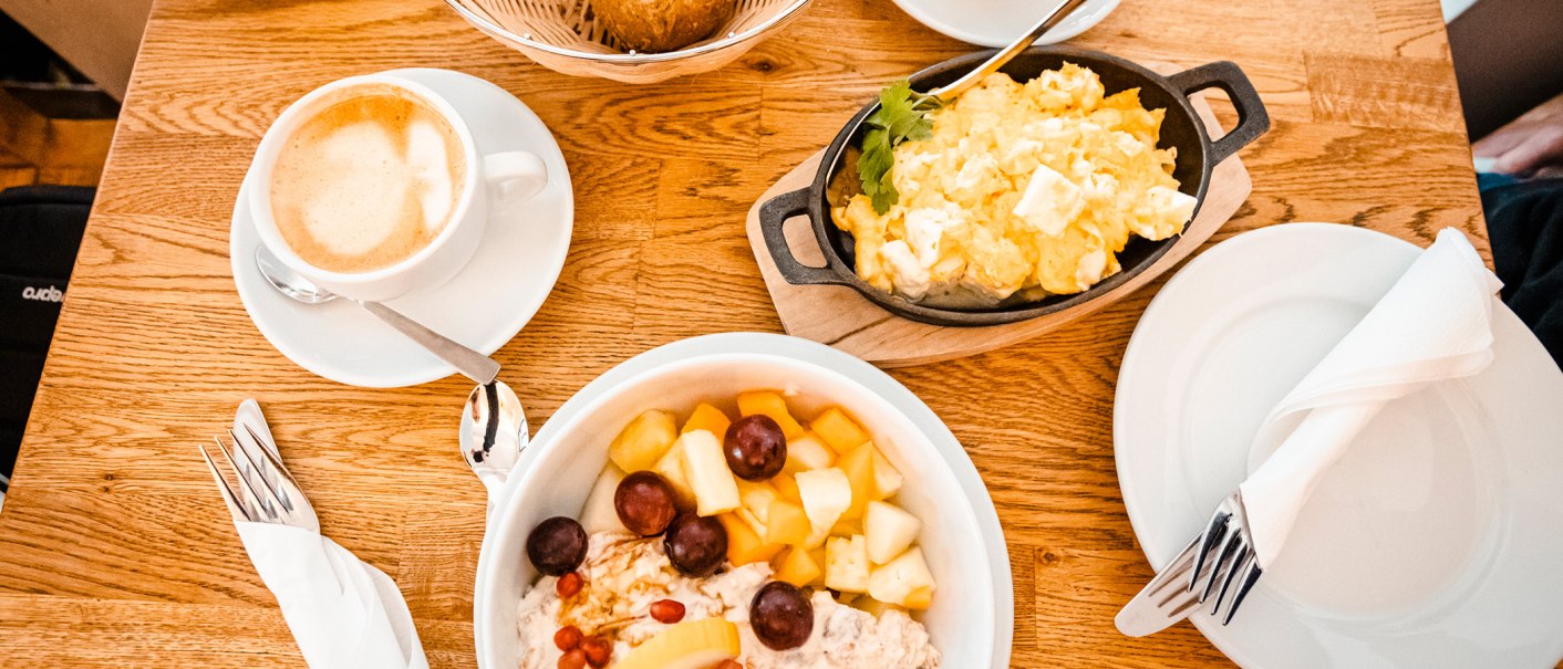 Ein Frühstückstisch mit einer Tasse Kaffee, Rührei in einer Pfanne und einem Obstsalat in einer Schüssel auf einem Holztisch., © Stuttgart-Marketing GmbH, Sarah Schmid