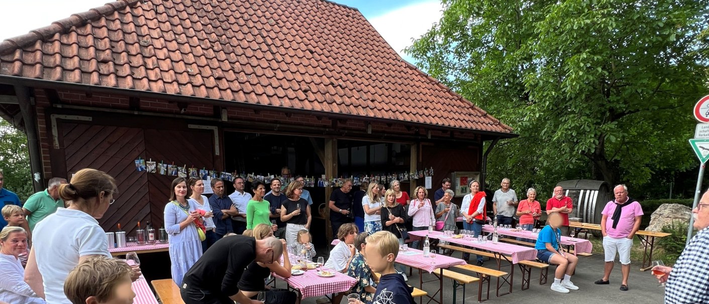 Eine Gruppe von Menschen steht und sitzt bei einem Fest vor einem Geb&auml;ude mit Ziegeldach. Es gibt B&auml;nke mit rot-wei&szlig; karierten Tischdecken., &copy; Frank Nonnenmann