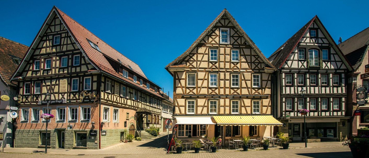 Half-timbered houses on Murrhardt’s market square under a clear blue sky. Tables and chairs from a café are set up in front of the buildings., © SMG Stuttgart Marketing GmbH - Sarah Schmid Half-timbered houses on Murrhardt’s market square under a clear blue sky. Tables and chairs from a café are set up in front of the buildings., © SMG Stuttgart Marketing GmbH - Sarah Schmid