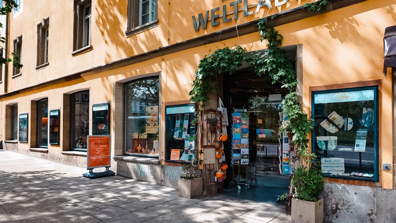 Au&szlig;enansicht des Weltladens Planie mit gelber Fassade, gro&szlig;en Fenstern und einem Eingang mit Pflanzen dekoriert., &copy; Michael Latz