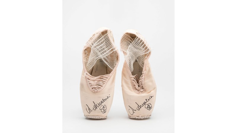 A pair of worn ballet pointe shoes with signatures on the toe, against a white background., &copy; Volker Naumann