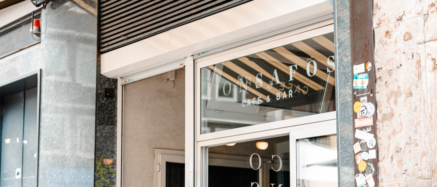 Entrance to a café with the inscription 'ConSafos Café & Bar' on the glass door. Next to it, a wall with stickers., © SMG Stuttgart Marketing GmbH - Sarah Schmid Entrance to a café with the inscription 'ConSafos Café & Bar' on the glass door. Next to it, a wall with stickers., © SMG Stuttgart Marketing GmbH - Sarah Schmid