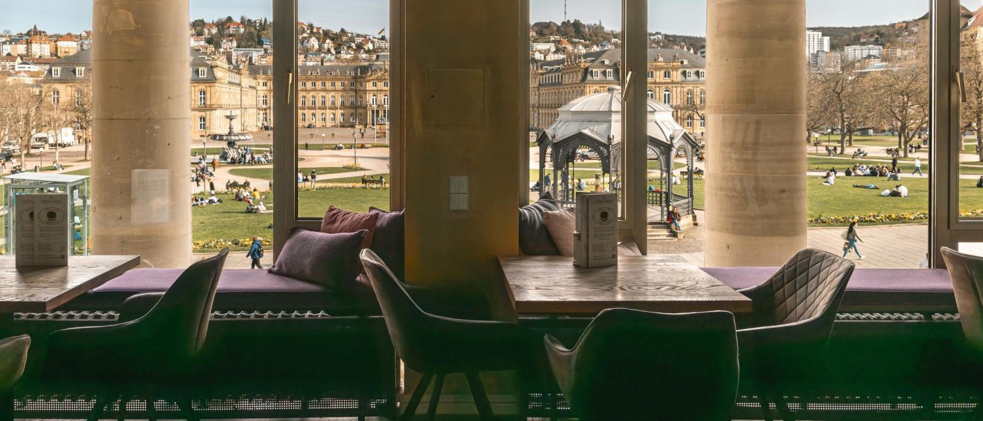 Blick aus dem Café Königsbau auf einen belebten Platz mit historischen Gebäuden und einem Pavillon. Menschen entspannen auf der Wiese., © Stuttgart-Marketing GmbH, Sarah Schmid