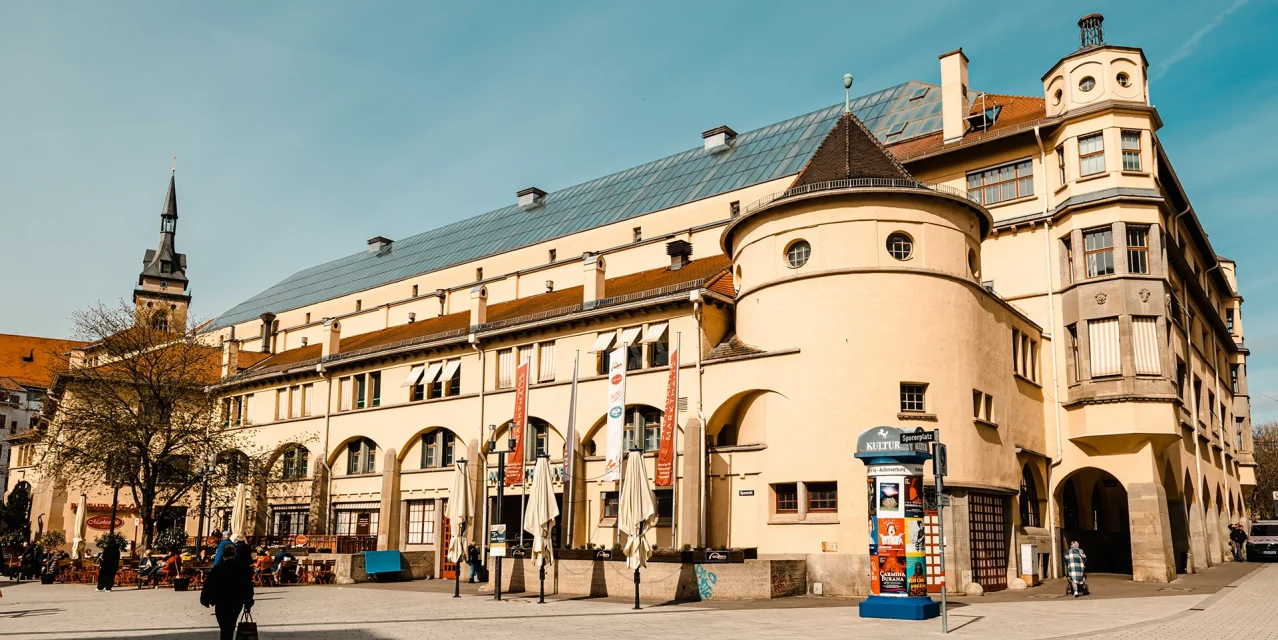 Die Markthalle am Sporerplatz mit Glasdach, Türmen und Außengastronomie an einem sonnigen Tag., © SMG, Sarah Schmid Die Markthalle am Sporerplatz mit Glasdach, Türmen und Außengastronomie an einem sonnigen Tag., © SMG, Sarah Schmid