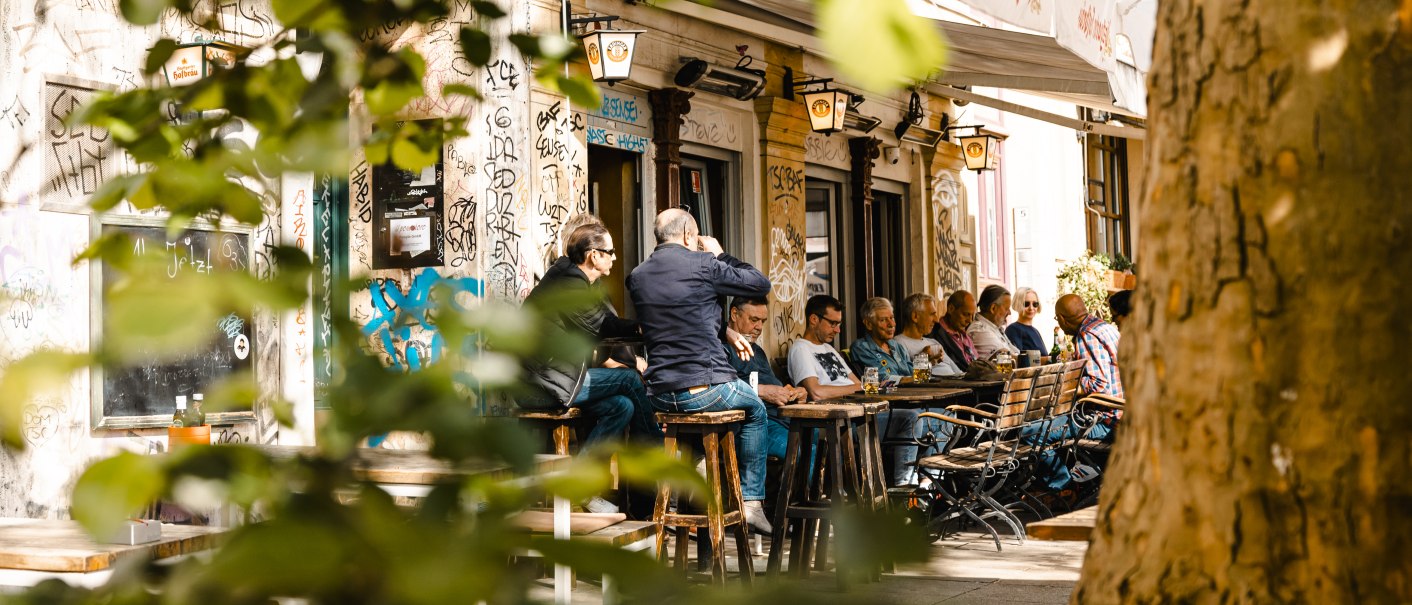 Menschen sitzen im Außenbereich eines Cafés namens La Concha, umgeben von Graffiti und Bäumen. Die Szene wirkt lebendig und entspannt., © SMG Stuttgart Marketing GmbH - Sarah Schmid