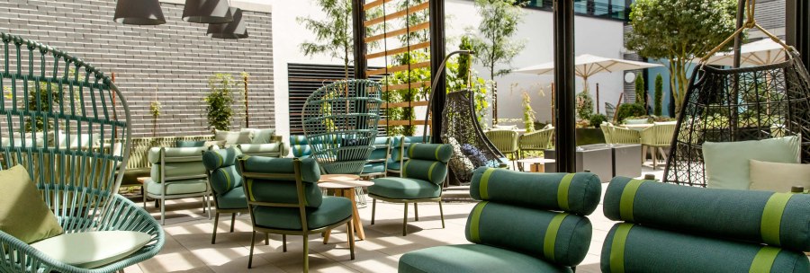Modern terrace with green seating furniture, wooden pergola and plants. Hanging chairs and tables create an inviting outdoor atmosphere., &copy; Motel One - Stuttgart Hauptbahnhof