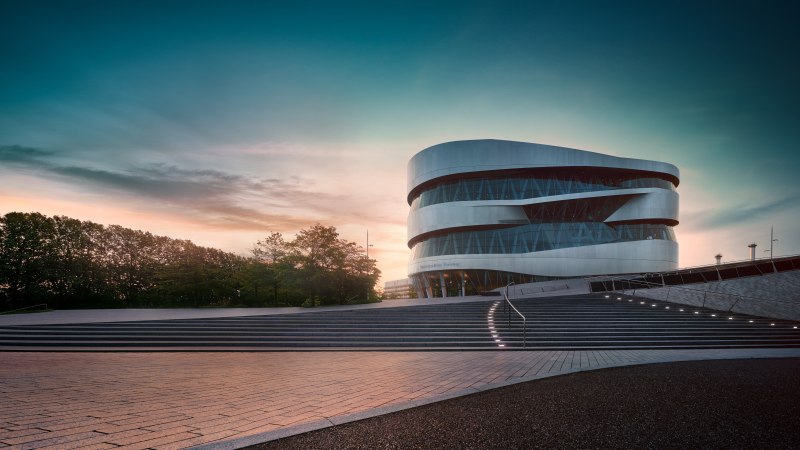 Das Mercedes-Benz Museum in Stuttgart bei Sonnenuntergang. Moderne Architektur mit geschwungenen Linien, umgeben von B&auml;umen und beleuchteten Stufen., &copy; Mercedes-Benz Heritage GmbH