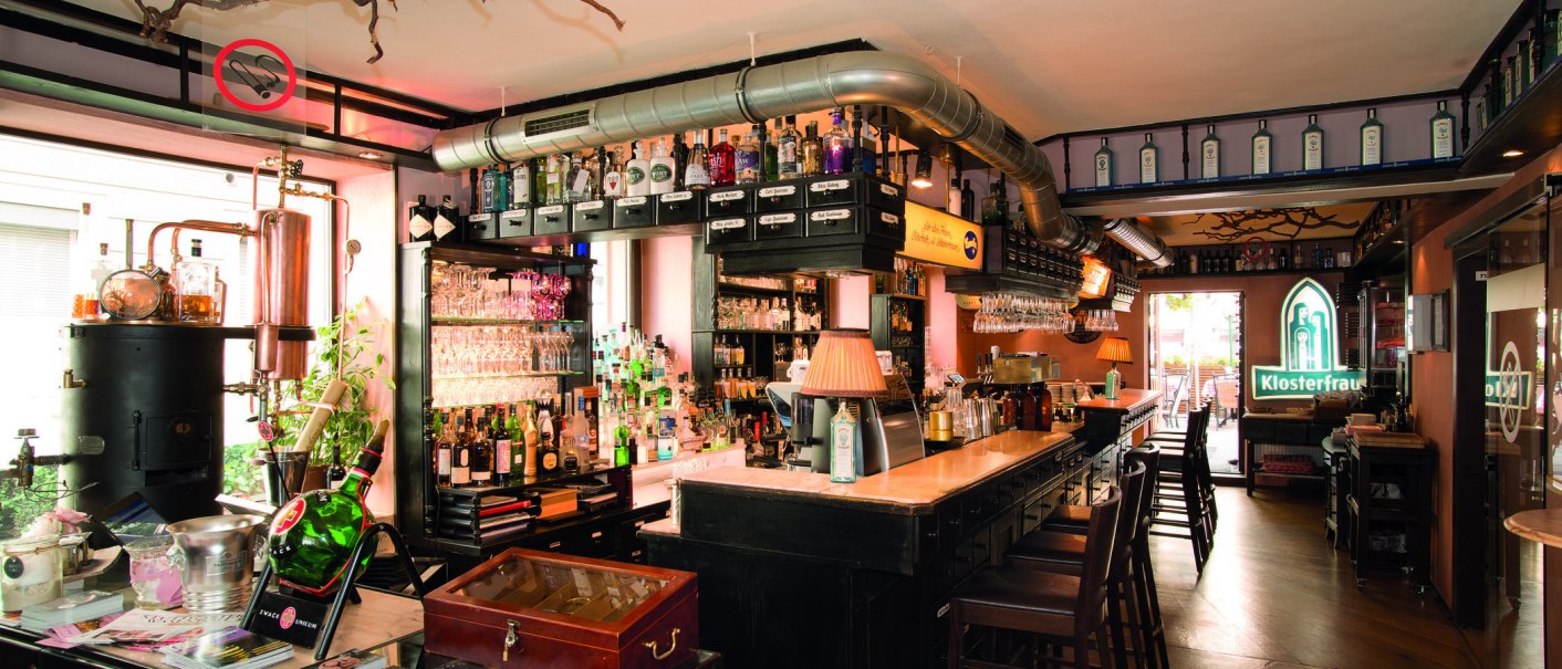 Bar mit Flaschen, Gläsern und Kupferdestille. Klosterfrau-Logo leuchtet im Hintergrund. Gemütliche Atmosphäre mit Holzmöbeln und Lampen., © Buschwerk Mediendesign-Wilhelmer Gastronomie