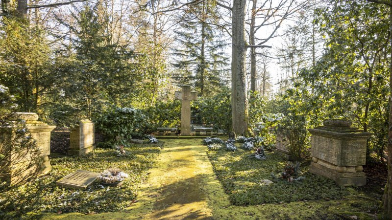 Ein ruhiger Friedhof mit einem gro&szlig;en Kreuz in der Mitte, umgeben von B&auml;umen und gr&uuml;ner Vegetation. Sonnenlicht f&auml;llt durch die Bl&auml;tter., &copy; Stuttgart-Marketing GmbH, Sarah Schmid