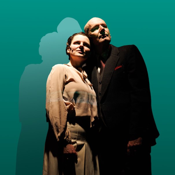 Ein Mann und eine Frau stehen eng beieinander vor einem gr&uuml;nen Hintergrund. Sie schauen nach oben, w&auml;hrend ihre Schatten hinter ihnen sichtbar sind., &copy; Theater der Altstadt
