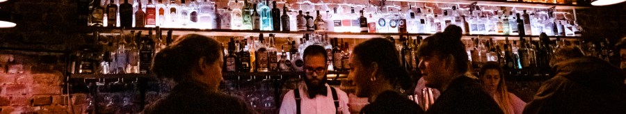 An atmospheric bar with illuminated bottle racks. People chat while a bartender prepares drinks., &copy; Stuttgart-Marketing GmbH, Sarah Schmid
