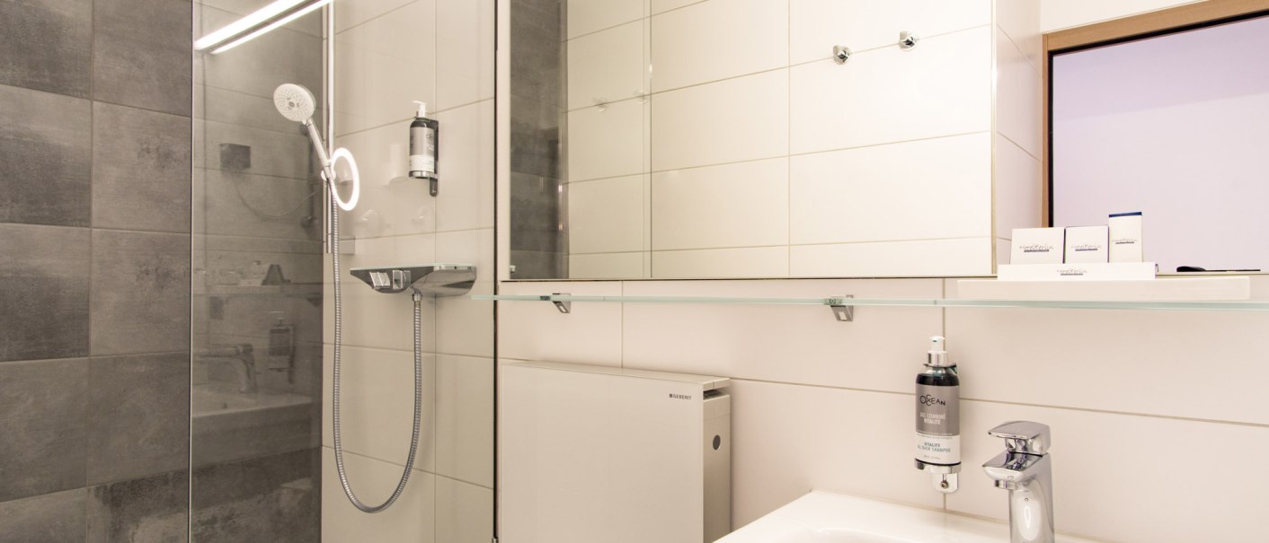 Modern bathroom with gray tiles, a glass shower, a sink, and a mirror. Subtle lighting and toiletries are provided., &copy; Hotel Berlin aZIS Hotel BetriebsGmbH