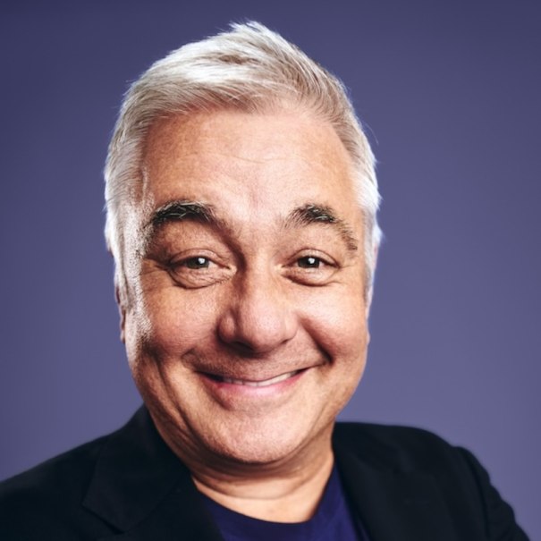 Ein Mann mit grauen Haaren l&auml;chelt in die Kamera. Er tr&auml;gt ein dunkles Oberteil. Der Hintergrund ist lila., &copy; Renitenztheater Stuttgart e.V.