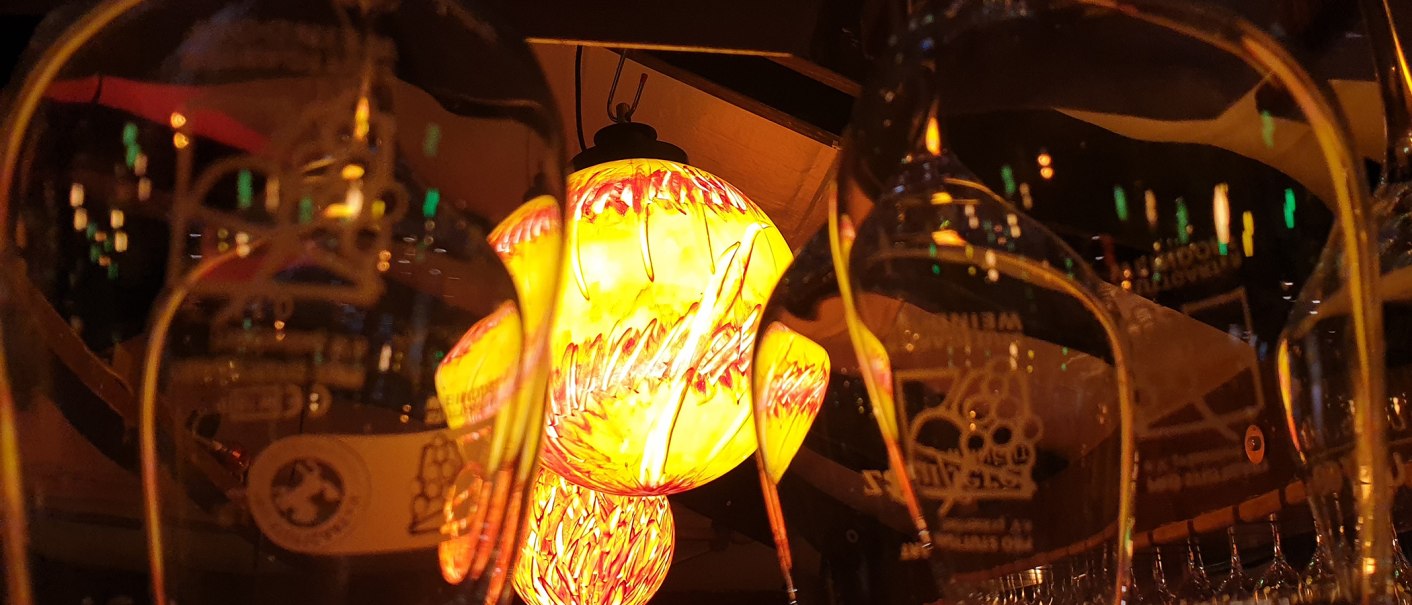 Weingläser reflektieren eine gelb-rote Lampe, die warmes Licht ausstrahlt. Die Szene wirkt gemütlich und einladend., © Weingut Ruoff