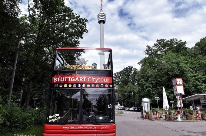 Roter Doppeldeckerbus der Stuttgart Citytour vor dem Stuttgarter Fernsehturm, umgeben von Bäumen und einem Café., © SMG, Pierre Polak