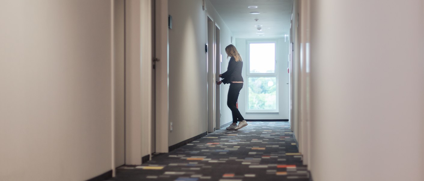 A person is standing in a long hallway and opens a door. The hallway is bright and has colorful carpeting., © the niu Form - Novum Hospitality A person is standing in a long hallway and opens a door. The hallway is bright and has colorful carpeting., © the niu Form - Novum Hospitality