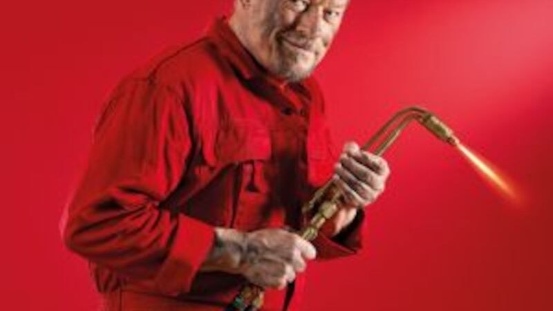 Ein &auml;lterer Mann in einem roten Overall h&auml;lt ein Schwei&szlig;ger&auml;t. Er tr&auml;gt eine Schutzbrille auf der Stirn. Der Hintergrund ist ebenfalls rot., &copy; Altes Schauspielhaus und Kom&ouml;die im Marquardt e.V.