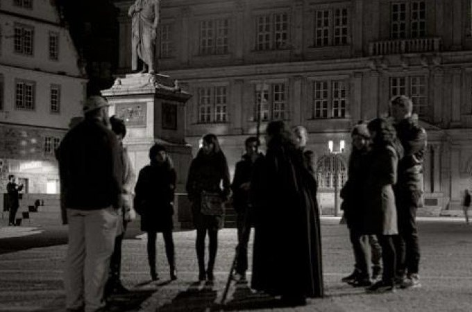 Eine Gruppe von Menschen steht nachts vor einer Statue auf einem Platz in Stuttgart. Die Szene wirkt geheimnisvoll und historisch., © Stuttgarter Geister