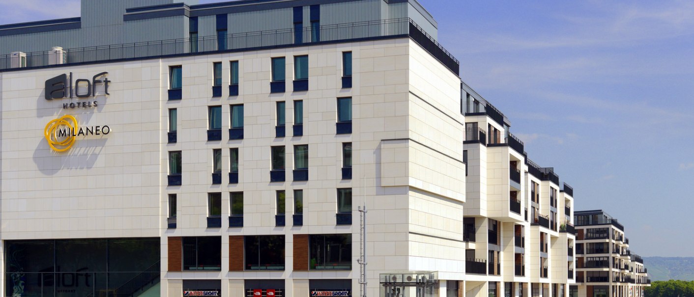 Modern building complex with hotel and stores, including brands such as Intersport and The North Face. Clean lines and bright fa&ccedil;ade., &copy; Aloft Stuttgart
