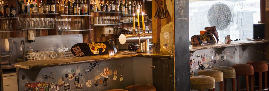 Eine gemütliche Bar mit Skateboard-Dekor auf der Theke, Kerzenleuchter und Barhockern. Im Hintergrund sind Flaschen und Gläser zu sehen., © Mata Hari, Stuttgart