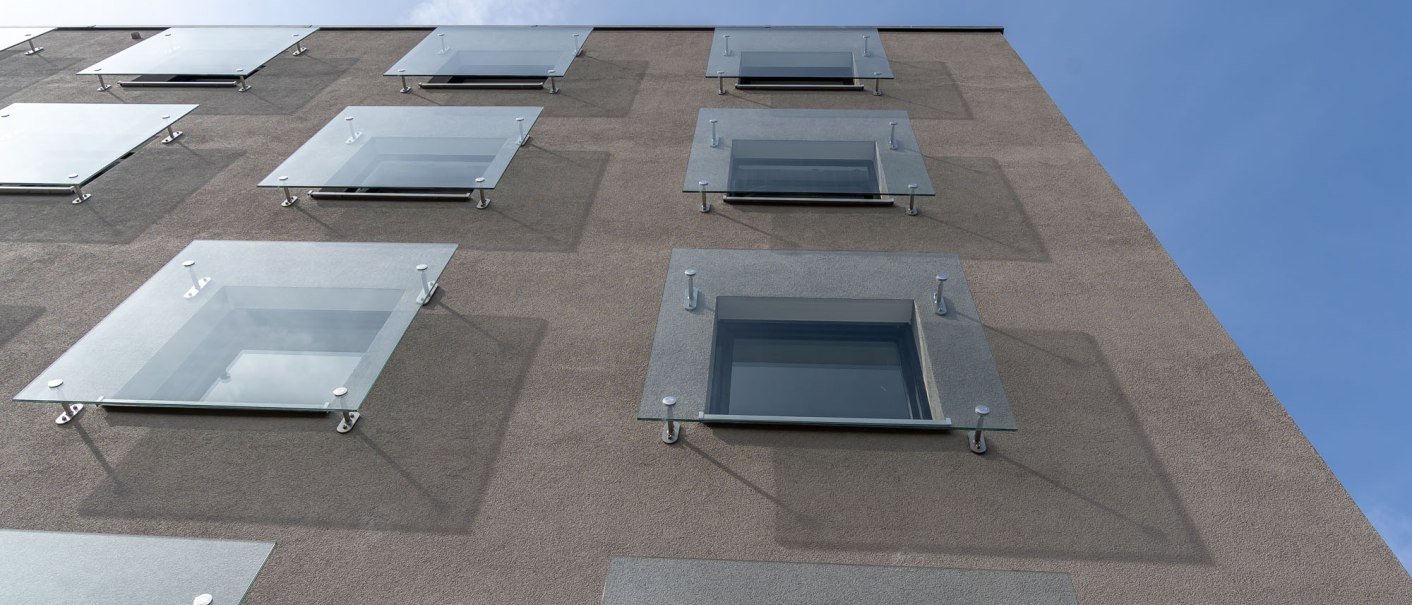 Modern building façade with glass canopies above the windows, arranged in a geometric pattern. Blue sky in the background., © a2 HOTELS