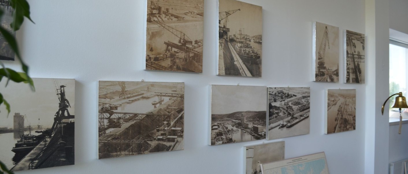 Mehrere historische Hafenfotos hängen an einer weißen Wand. Eine Pflanze und eine goldene Glocke sind im Vordergrund sichtbar., © Stuttgart-Marketing GmbH