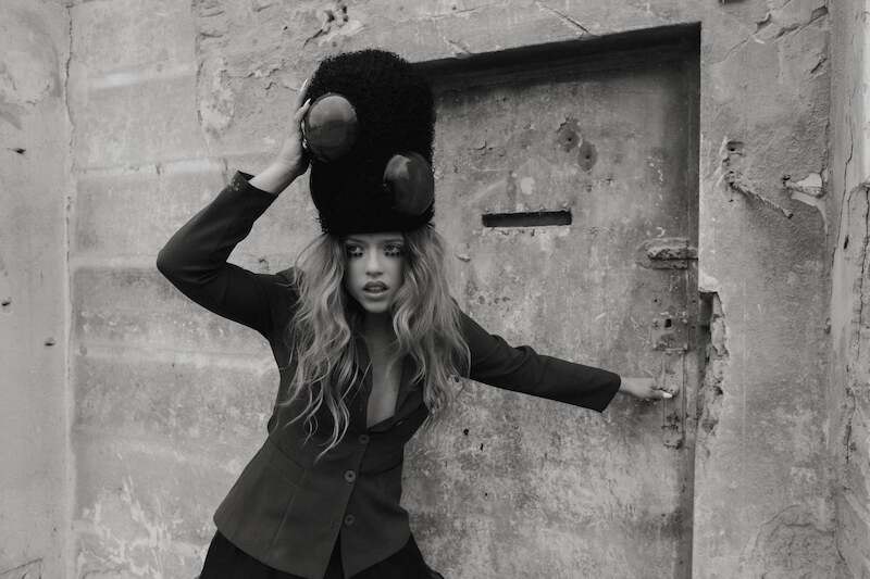 Eine Frau mit einem großen, flauschigen Hut posiert vor einer alten, verwitterten Tür. Sie trägt einen Blazer und hat langes, gewelltes Haar., © Music Circus Concertbüro GmbH & Co. KG Eine Frau mit einem großen, flauschigen Hut posiert vor einer alten, verwitterten Tür. Sie trägt einen Blazer und hat langes, gewelltes Haar., © Music Circus Concertbüro GmbH & Co. KG